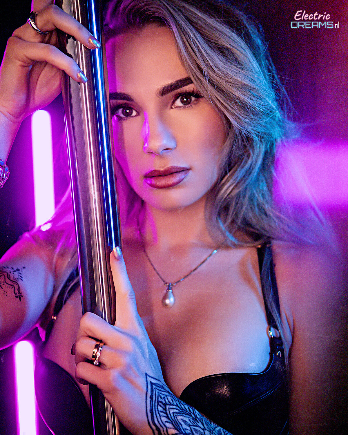 The image shows a woman in a black dress holding a pole in front of a neon light, with a watermark in the top right corner.