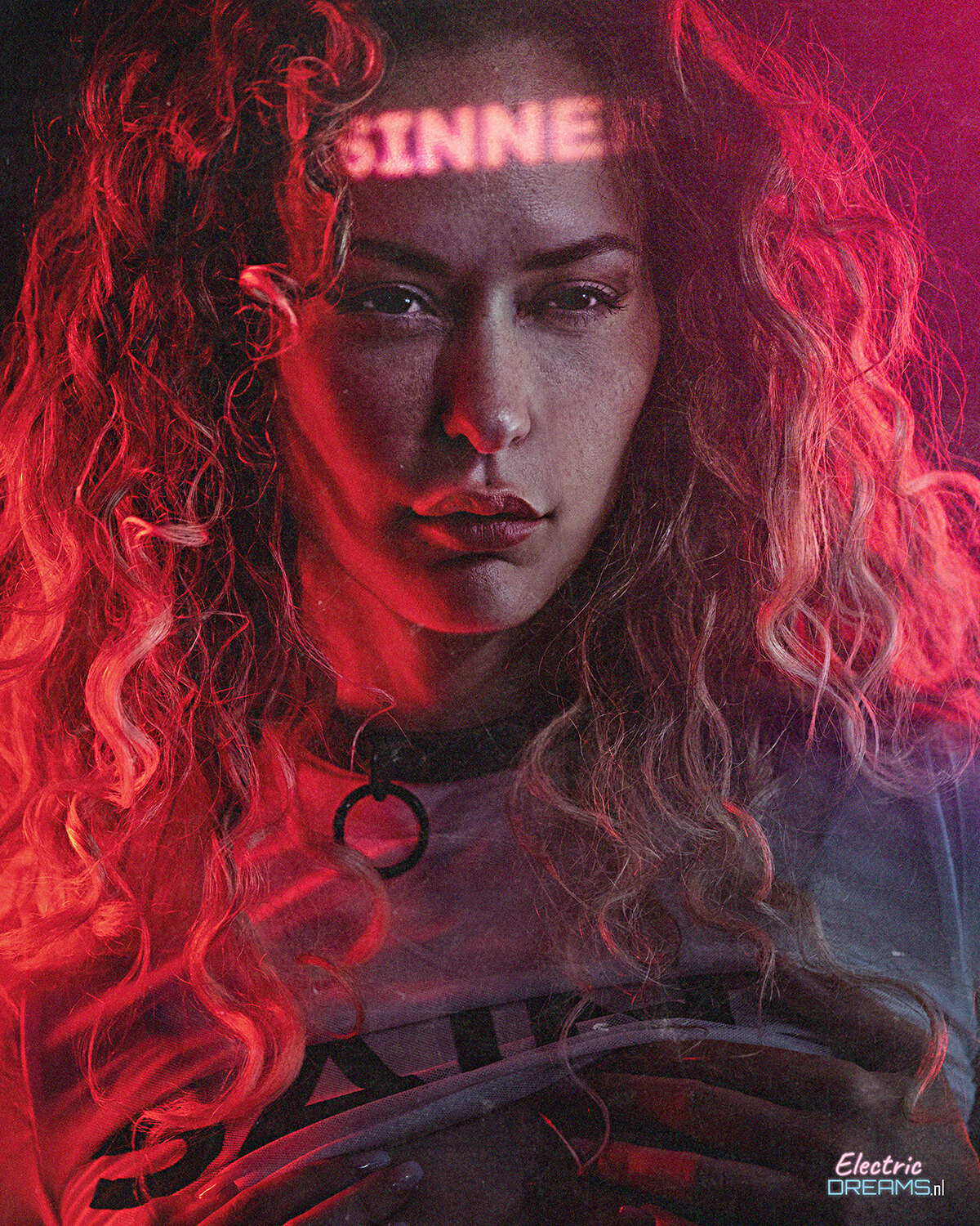 The image shows a woman with long red hair wearing a t-shirt with something written on it, and a watermark in the bottom right corner.