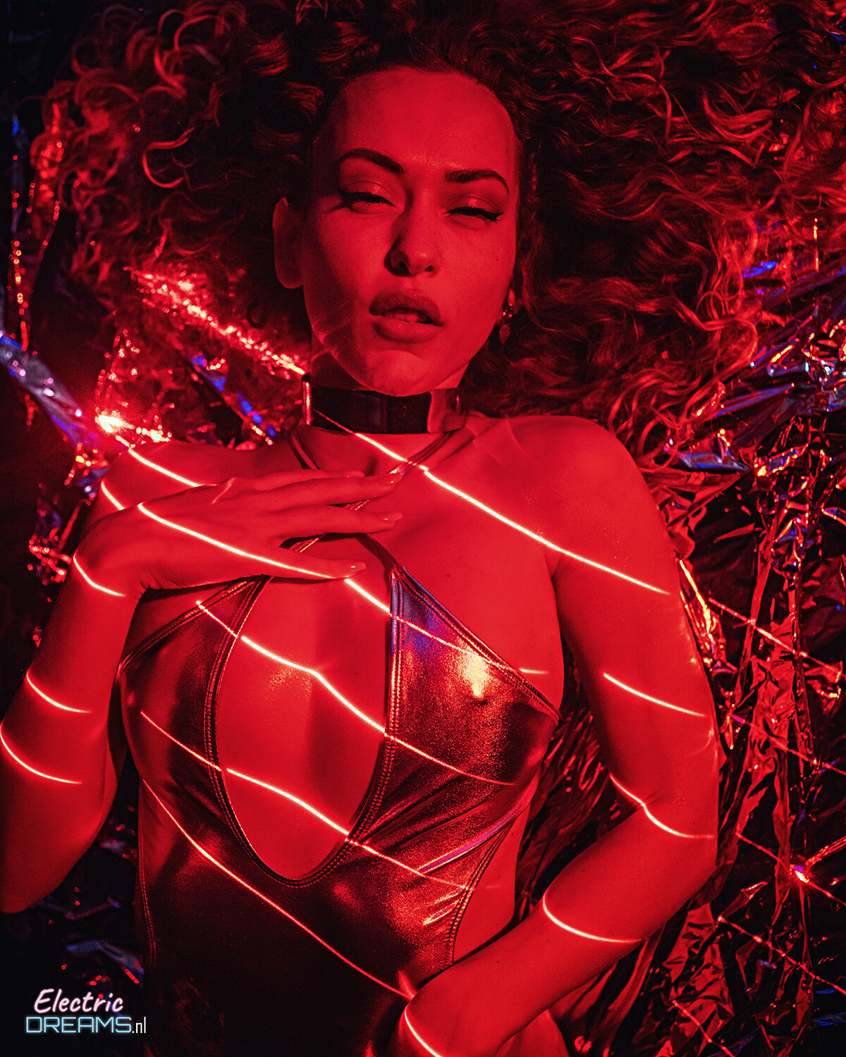 The image shows a woman in a black dress with red lights on her body, standing in front of a dark background with some decorative items.