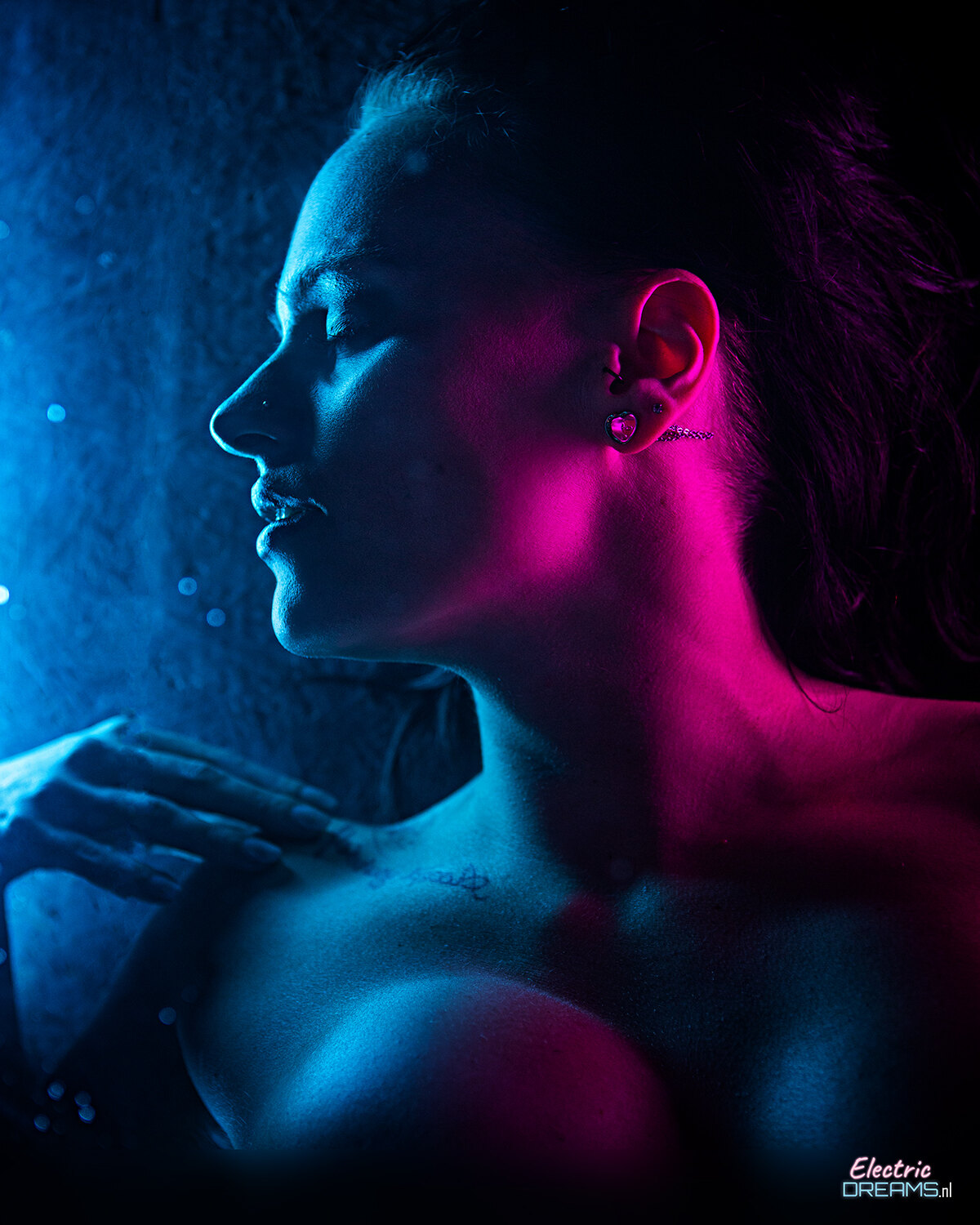 The image shows a woman with her face illuminated by a blue light, standing in front of a wall with text at the bottom.