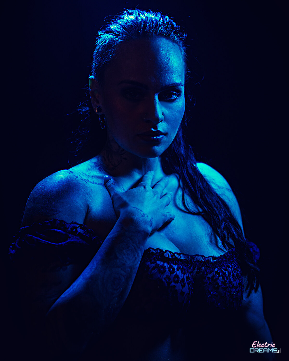 The image shows a woman in a black lingerie posing for a picture against a dark background with a watermark in the bottom right corner.