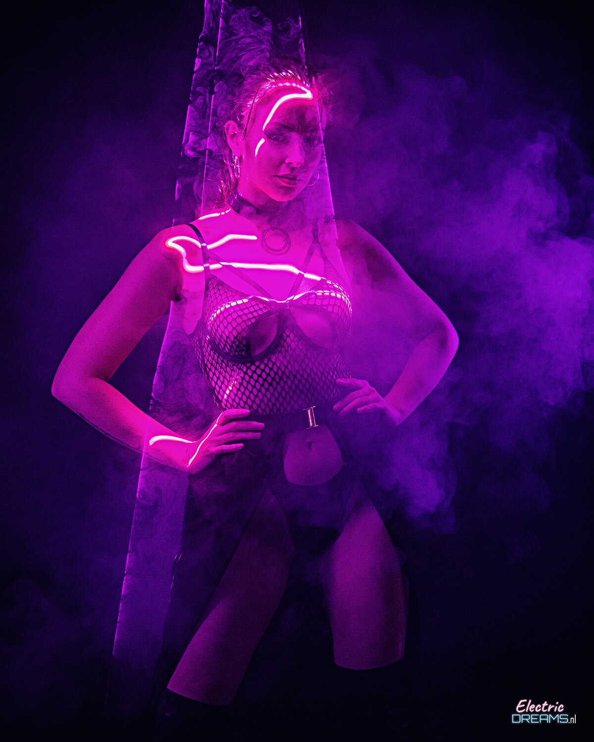 The image shows a woman standing in the center of a dark background, illuminated by a purple light.