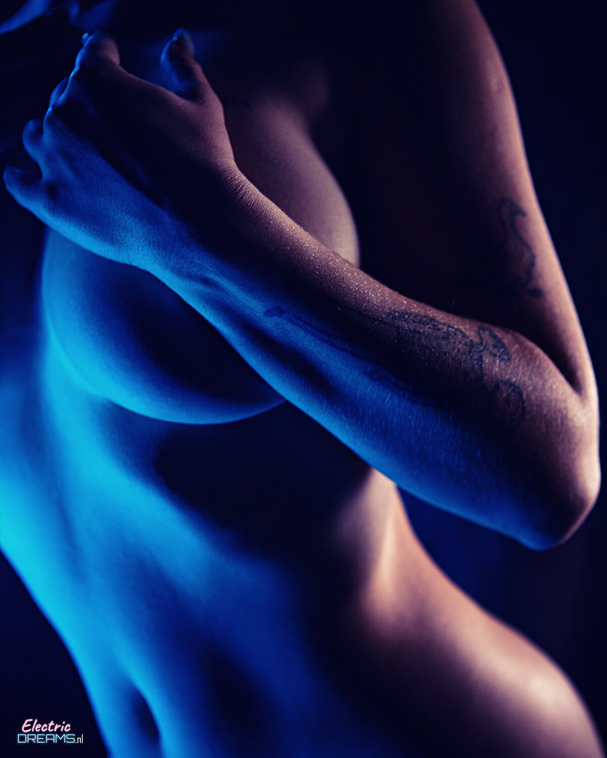 The image shows a woman with a tattoo on her arm against a dark background, with text at the bottom.