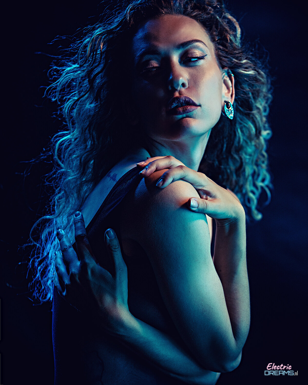 The image shows a woman with long curly hair wearing a black dress against a dark background, with text at the bottom.