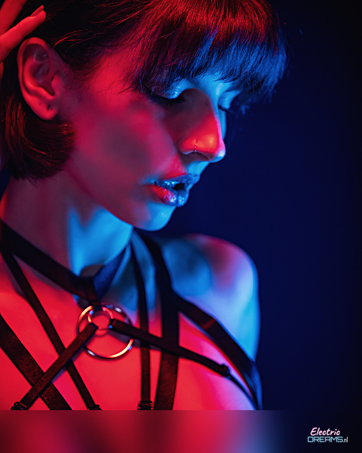 The image shows a woman with red hair wearing a black dress and a necklace, her face illuminated against a dark background.