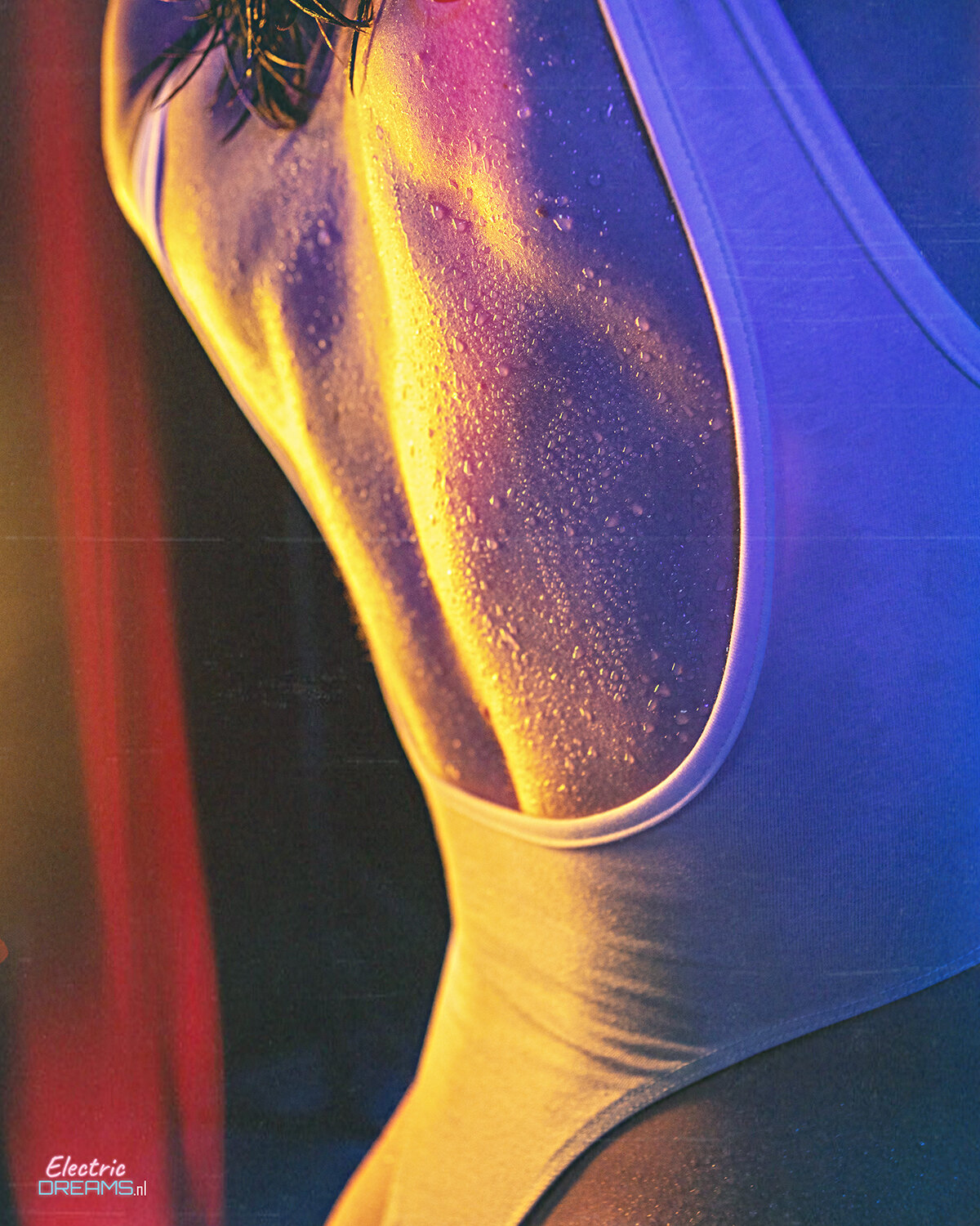 The image shows a woman in a blue and yellow swimsuit standing in front of a colorful background. She has a confident stance and her arms are outstretched, as if she is ready to take on the world. Her hair is pulled back in a ponytail and she has a determ