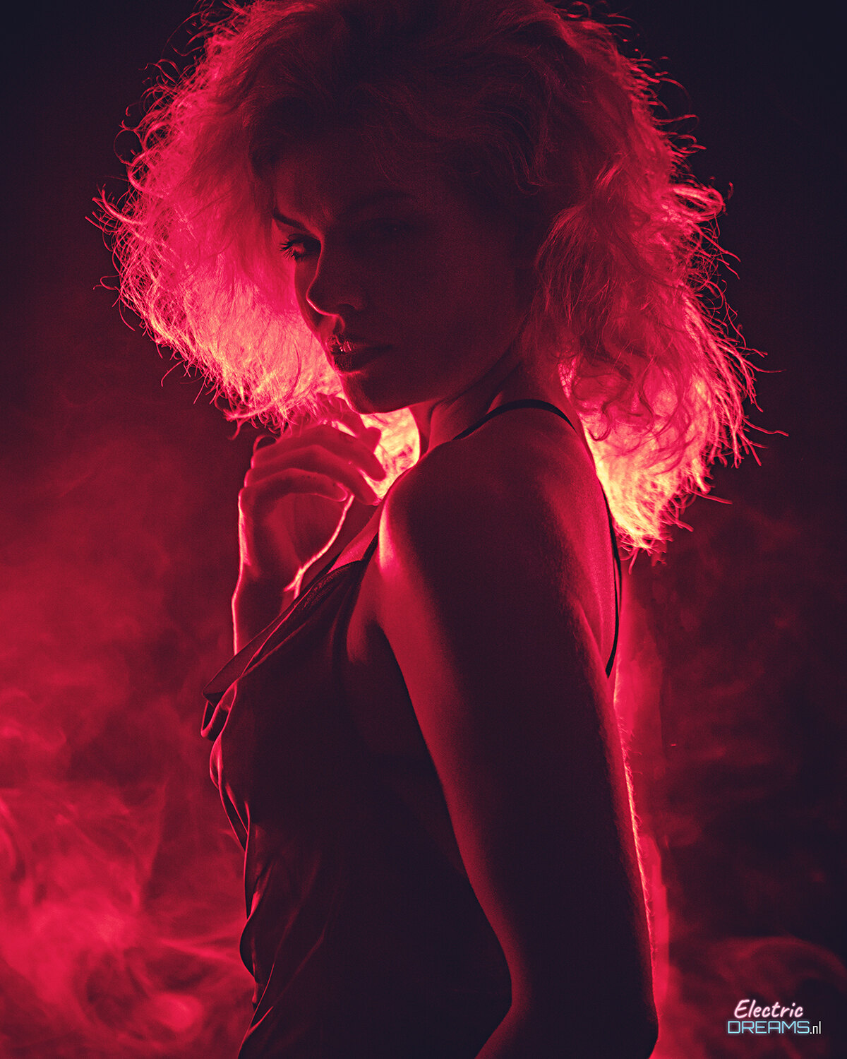 The image shows a woman in a black dress standing in front of a red light, with smoke in the background and a watermark on the image.