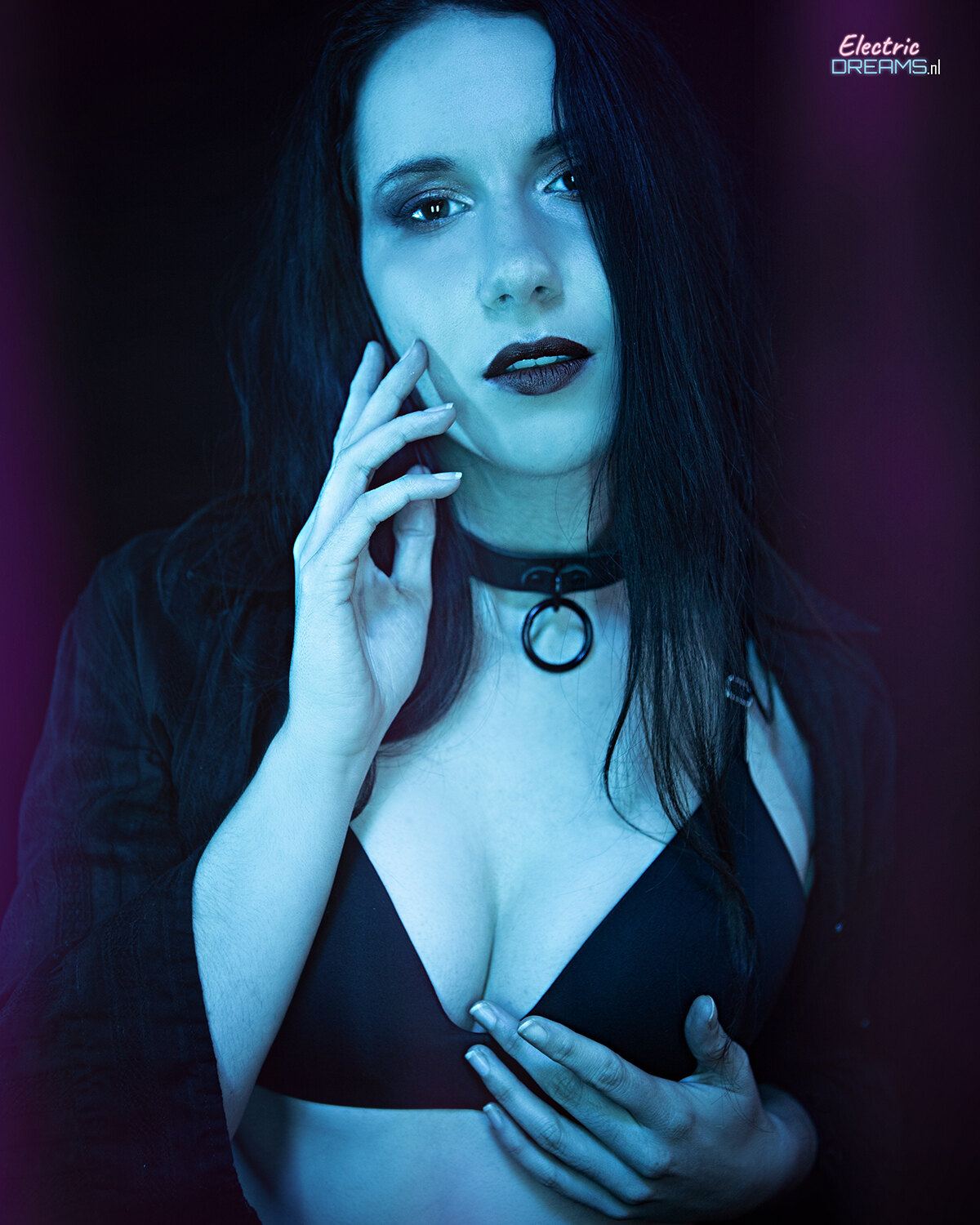 The image shows a woman in a black dress posing for a picture against a dark background with a watermark in the top right corner.