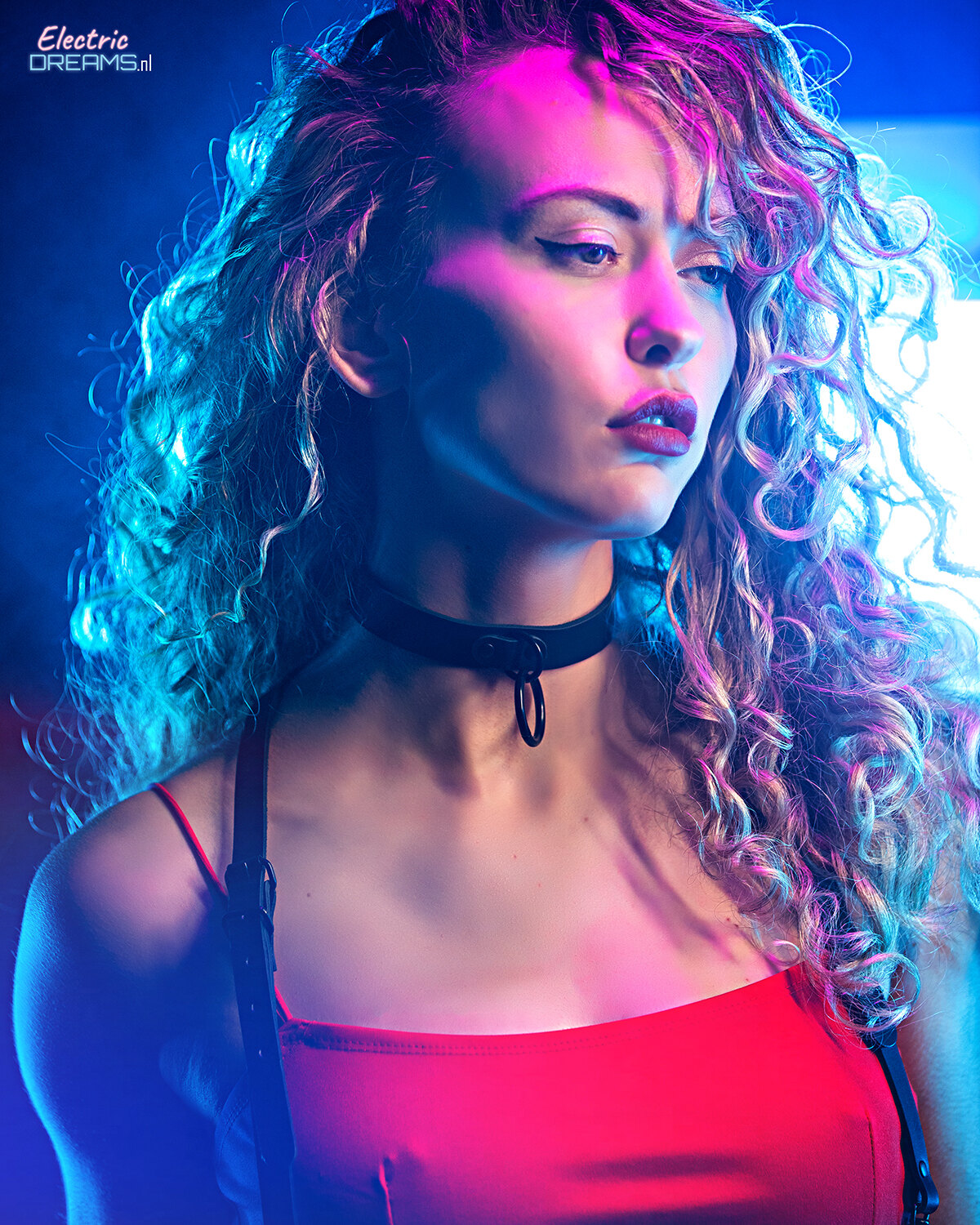 The image shows a woman with long curly hair wearing a red dress, illuminated by a light in the background.