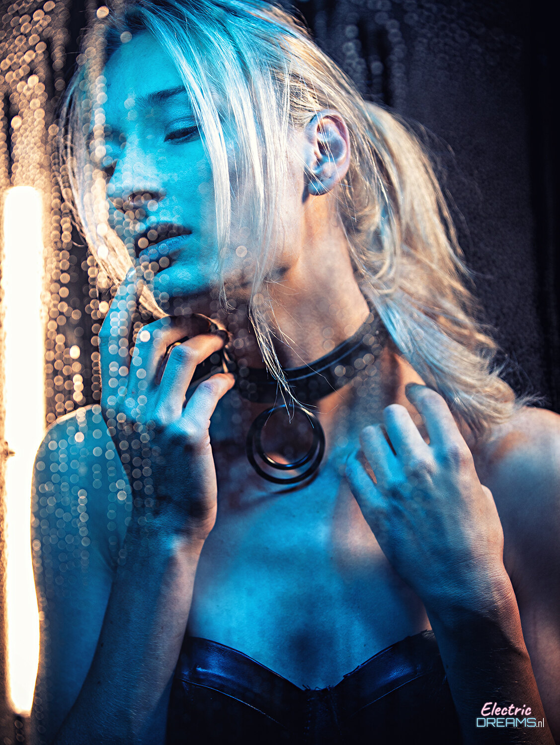 The image shows a woman in a black dress standing in front of a window, illuminated by a light on the left side and a curtain in the background.