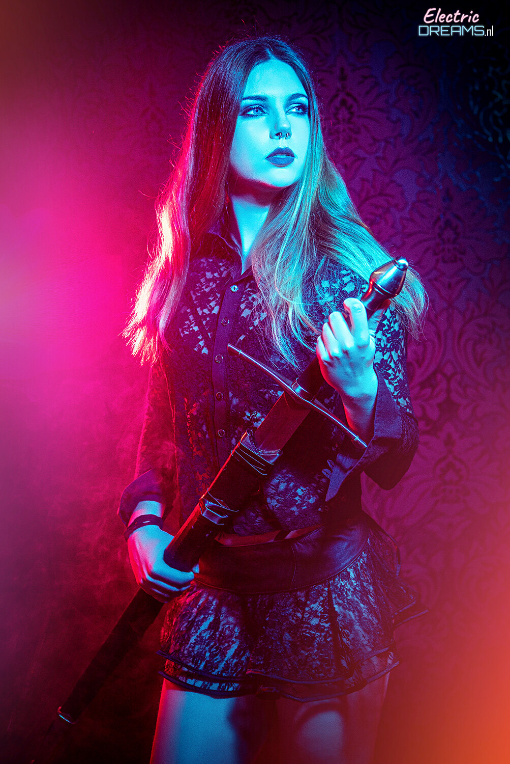 The image shows a woman standing and holding a gun in her hand, with a wall in the background and text at the top right corner.