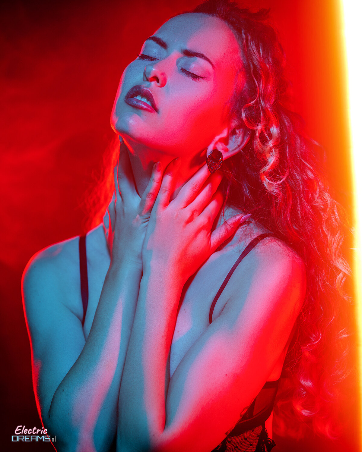 The image shows a woman with long red hair standing in front of a red light, with a watermark in the bottom left corner.