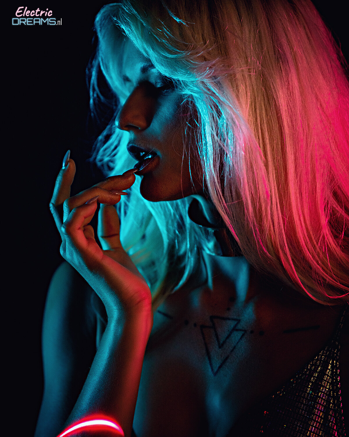The image shows a woman with pink hair and a tattoo on her chest, illuminated by a light in a dark background with a watermark.